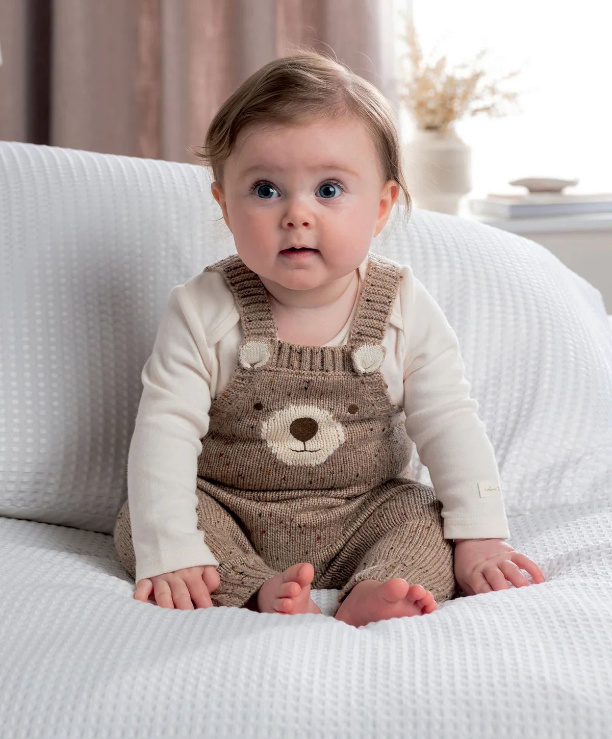 Baby wearing brown knitted bear dungarees with cream long-sleeve bodysuit, front bear face