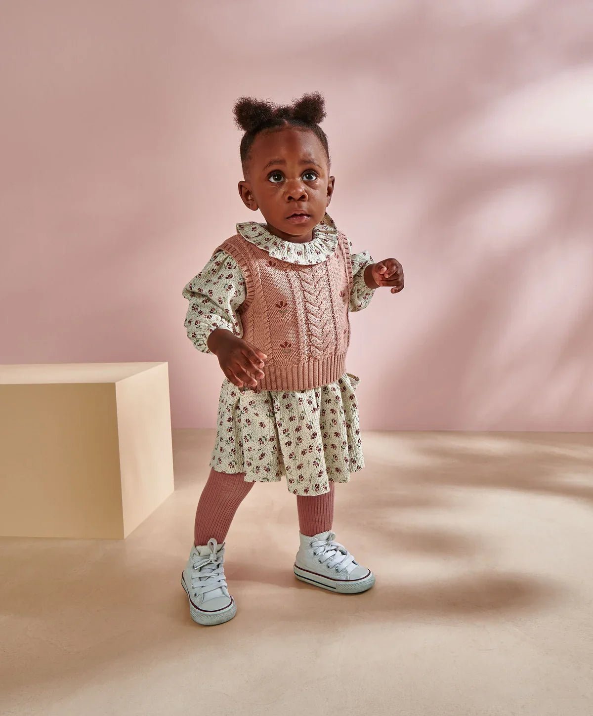 Two-piece floral dress and pink knit vest set on child with frilled neckline