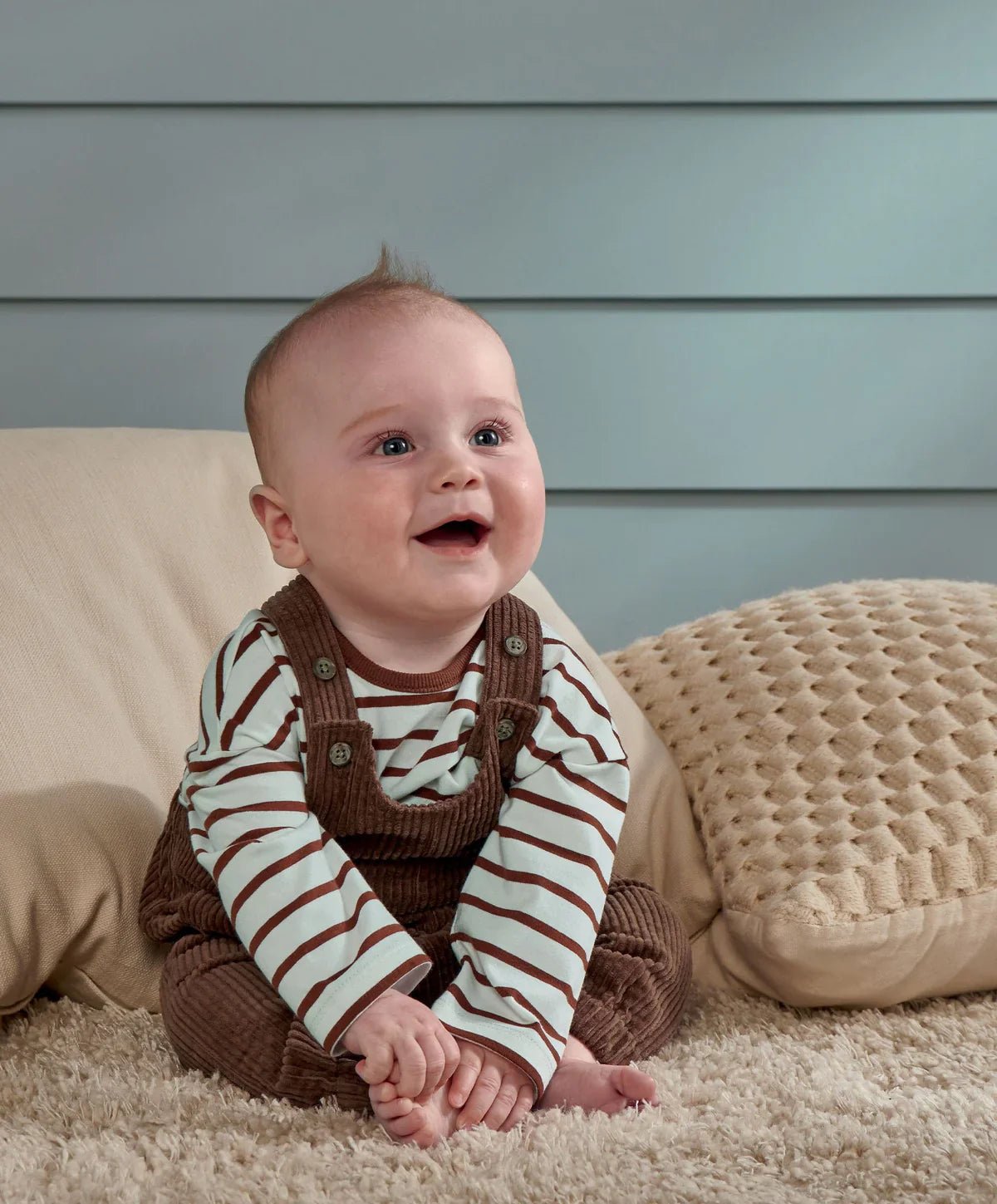 Baby wearing brown cord dungarees with a brown-and-white striped long-sleeve shirt
