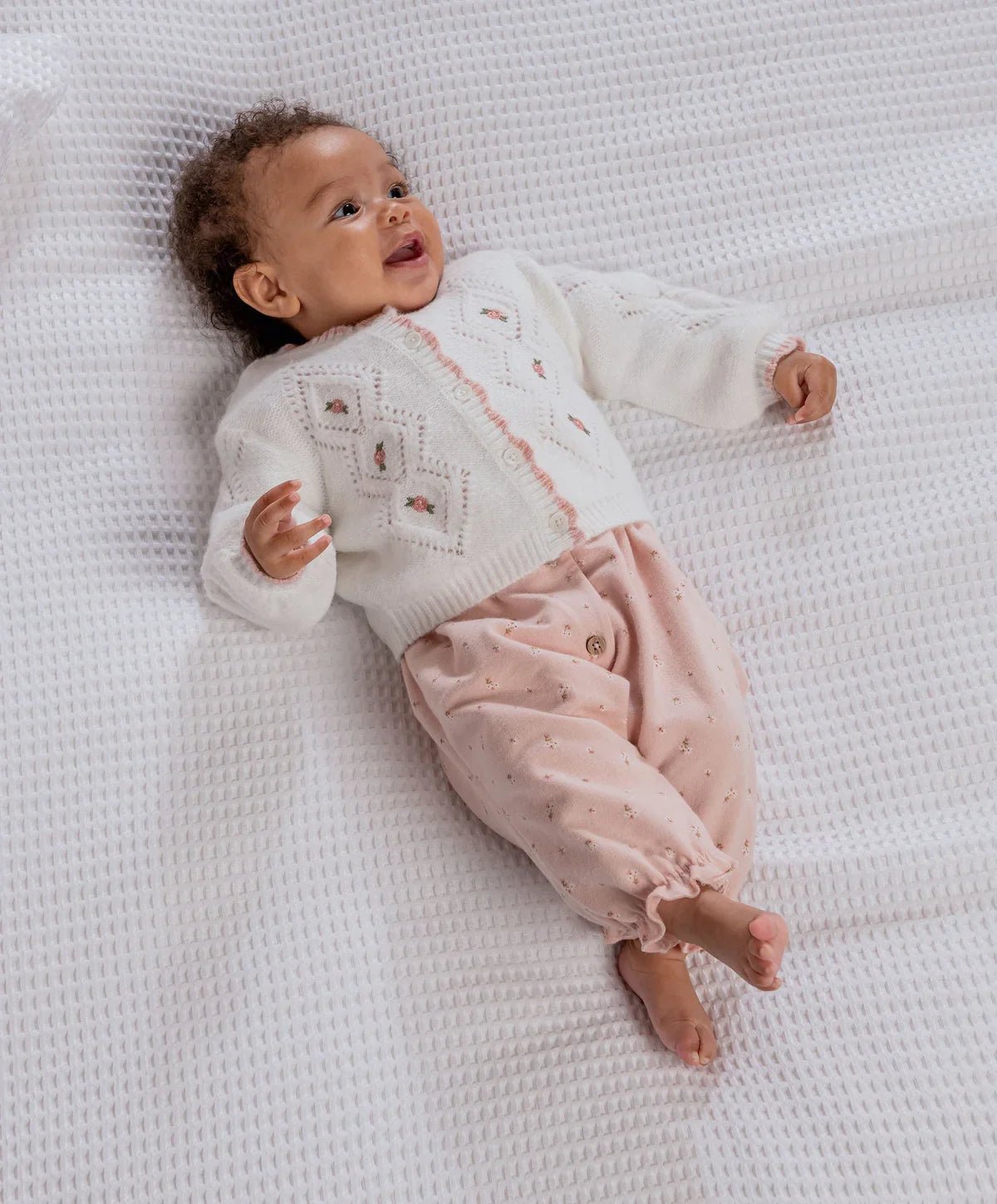 Baby wearing white embroidered cable knit cardigan with button front and floral accents