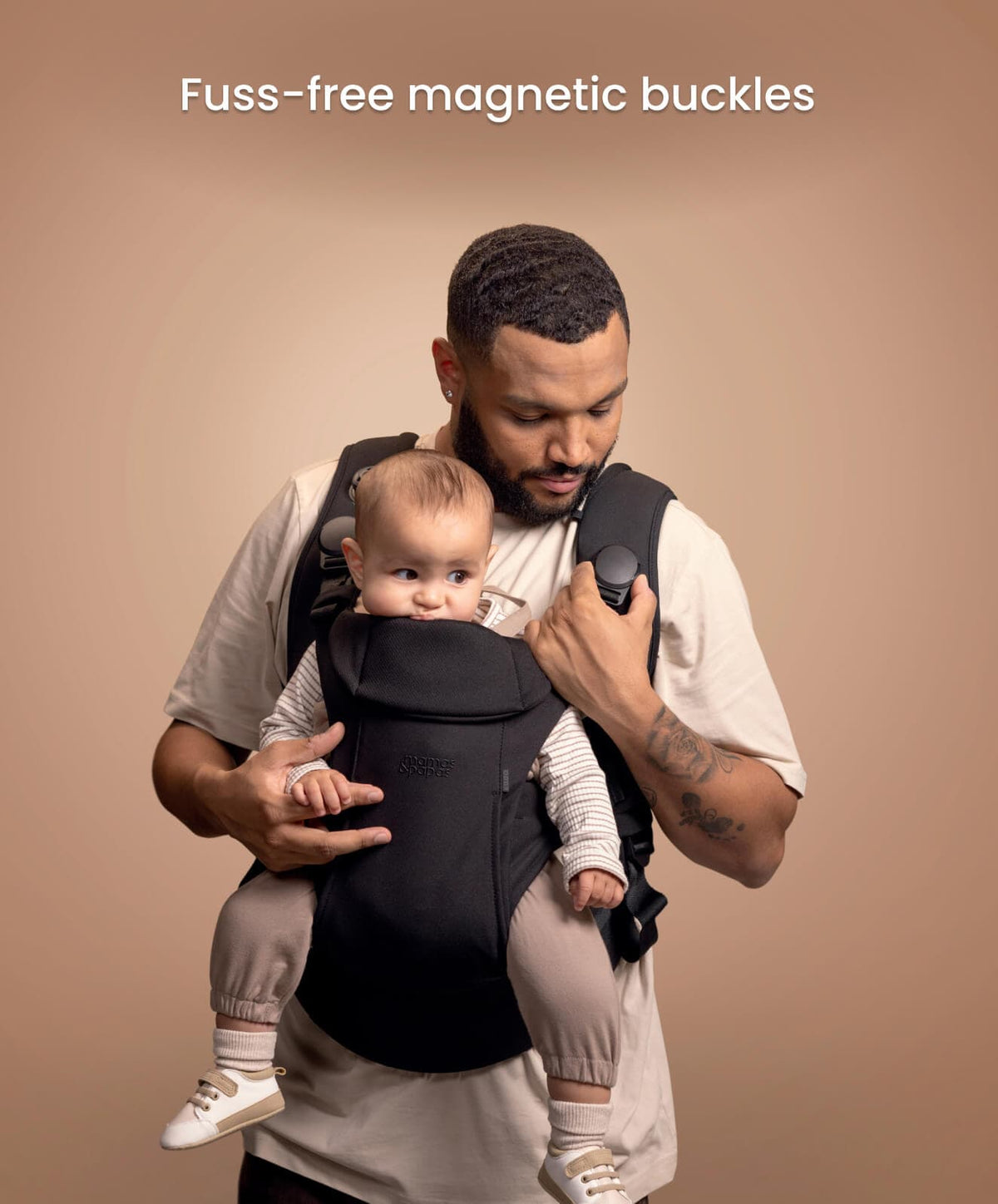 Black baby carrier with front buckle area, parent wearing it with seated baby