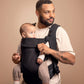 Black baby carrier with front panel, worn by parent holding seated infant
