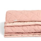 Folded baby quilt in light pink, showing layered quilted padding and stitched edge