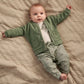Baby wearing green button jacket with pockets and green gingham trousers over a white bodysuit.