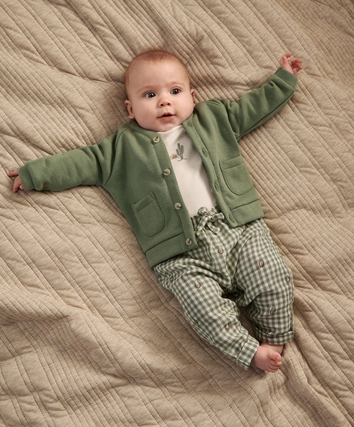 Baby wearing green button jacket with pockets and green gingham trousers over a white bodysuit.