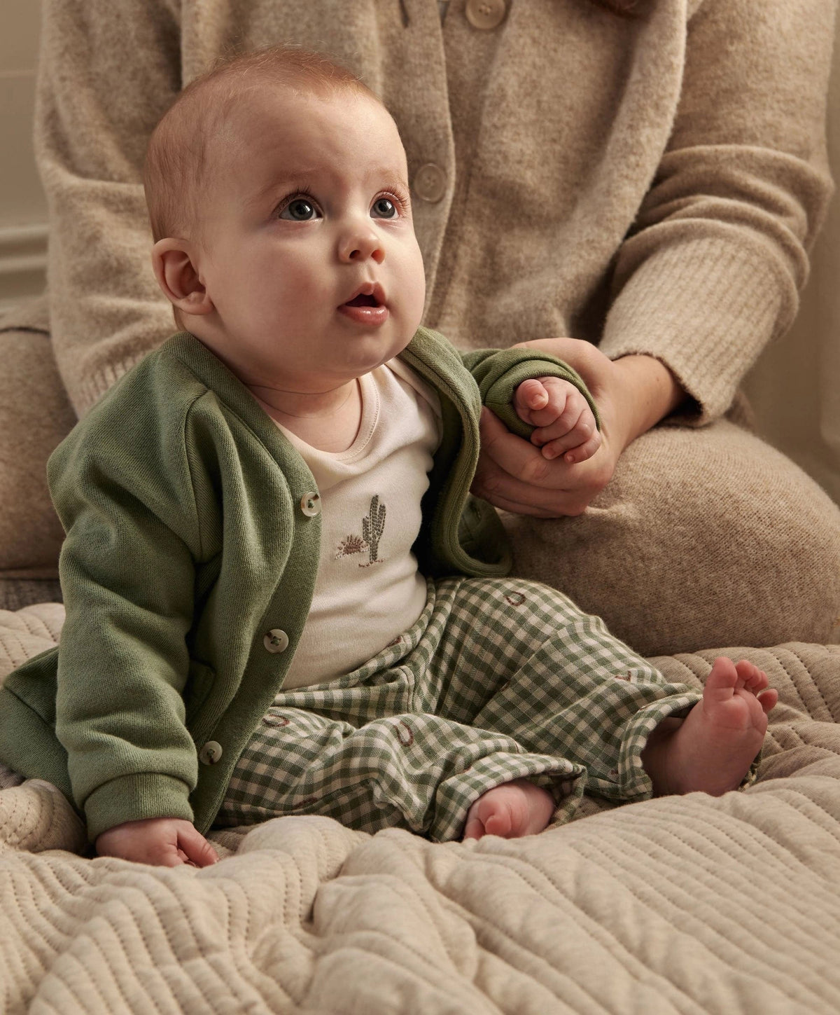 Baby in green button jacket with pockets, white bodysuit, and green gingham trousers.