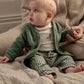 Baby reclining in green button jacket with pockets, white bodysuit, and green gingham trousers.