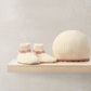 Cream knit booties and matching hat with pink ribbed trim, on display