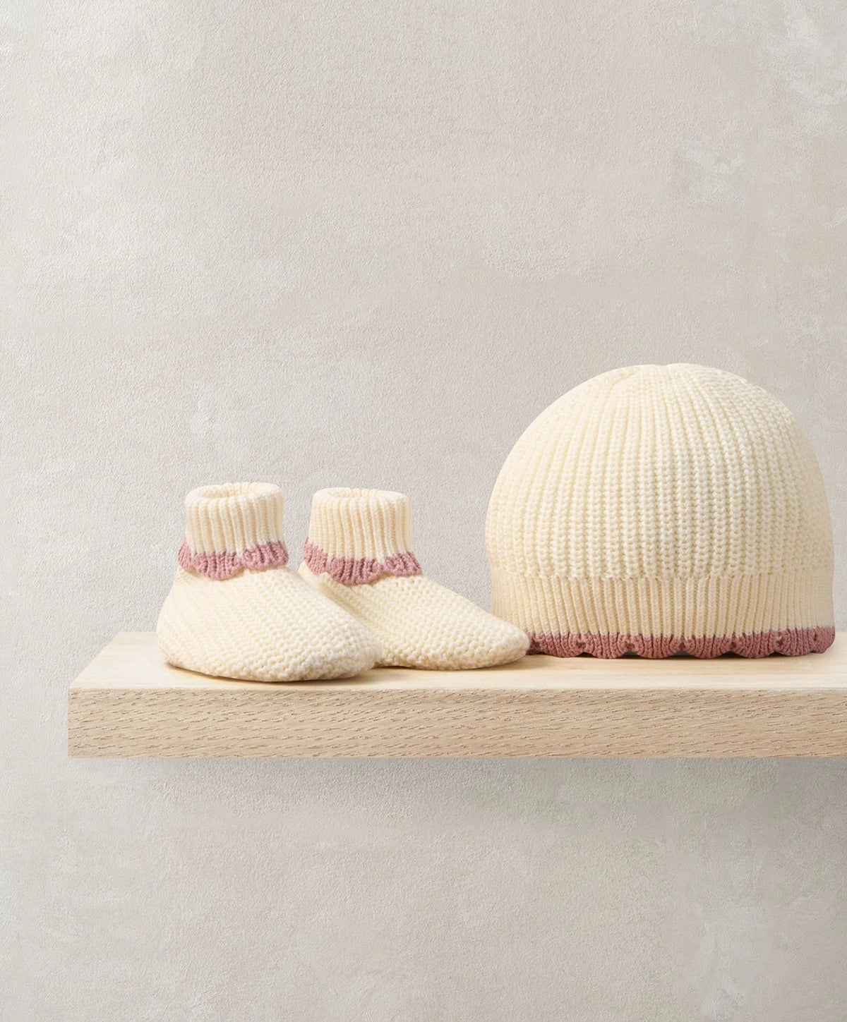 Cream knit booties and matching hat with pink ribbed trim, on display
