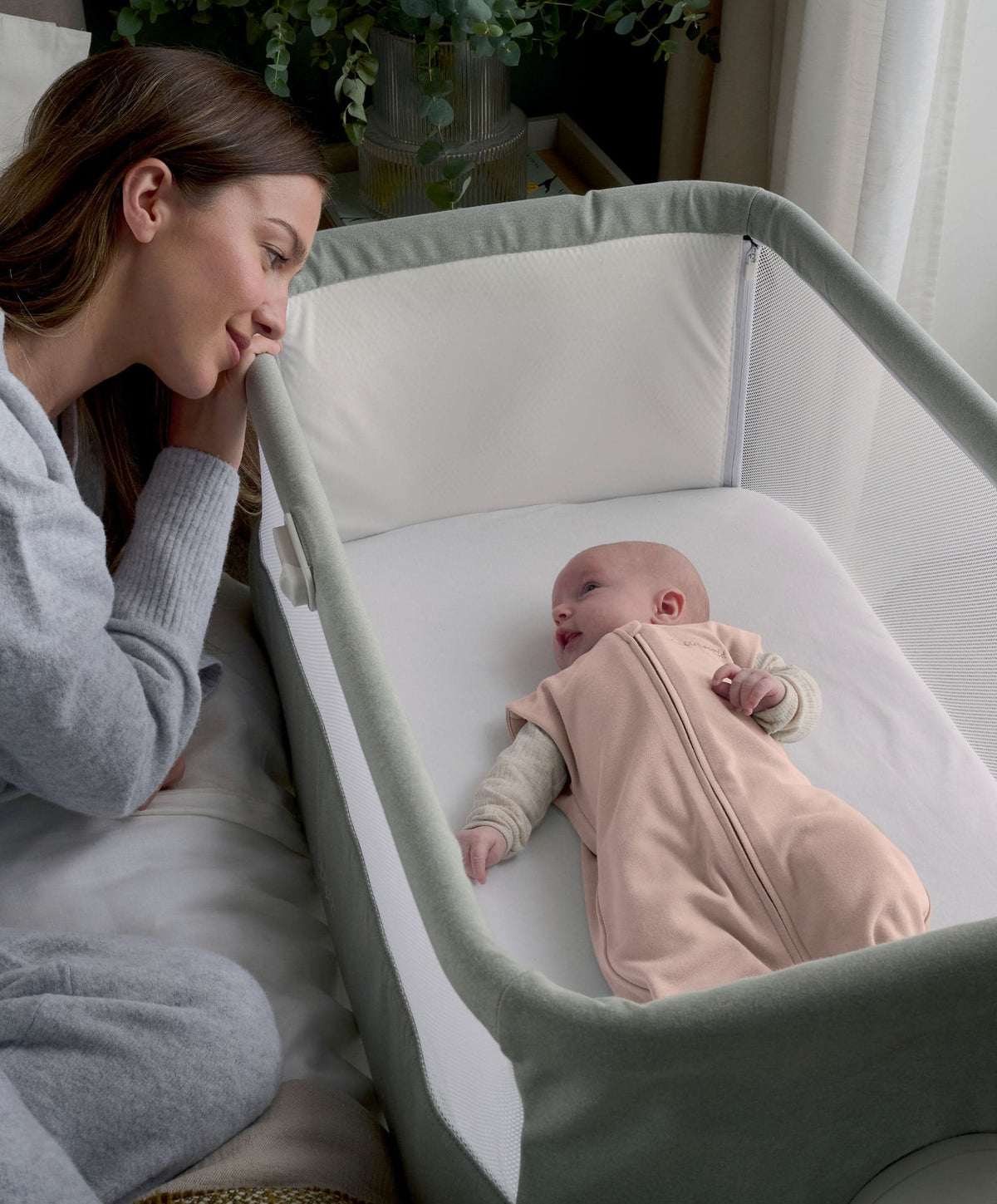 Pink zip-front swaddle sleeping bag on a baby in an open crib