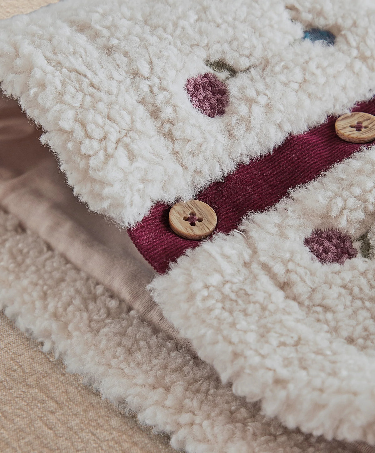 Cream sherpa with burgundy placket, embroidered motifs, and round wooden button