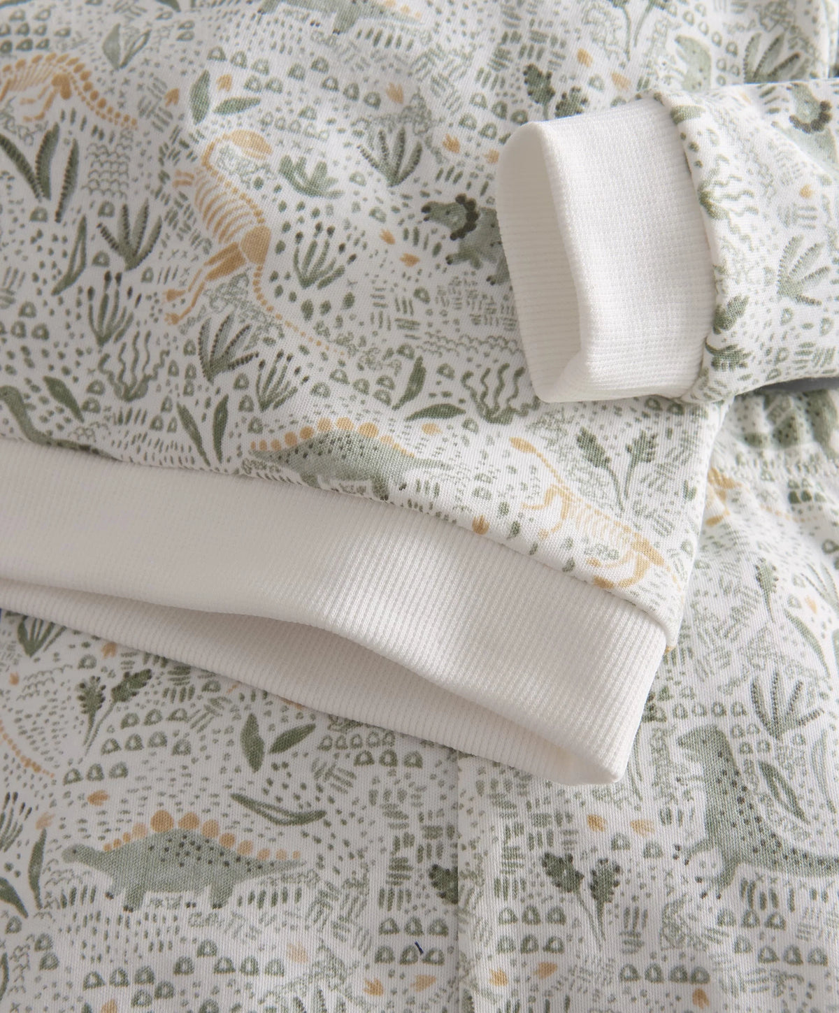 Dinosaur jersey pyjamas close-up: rib-knit cuffs and waistband, all-over dino pattern