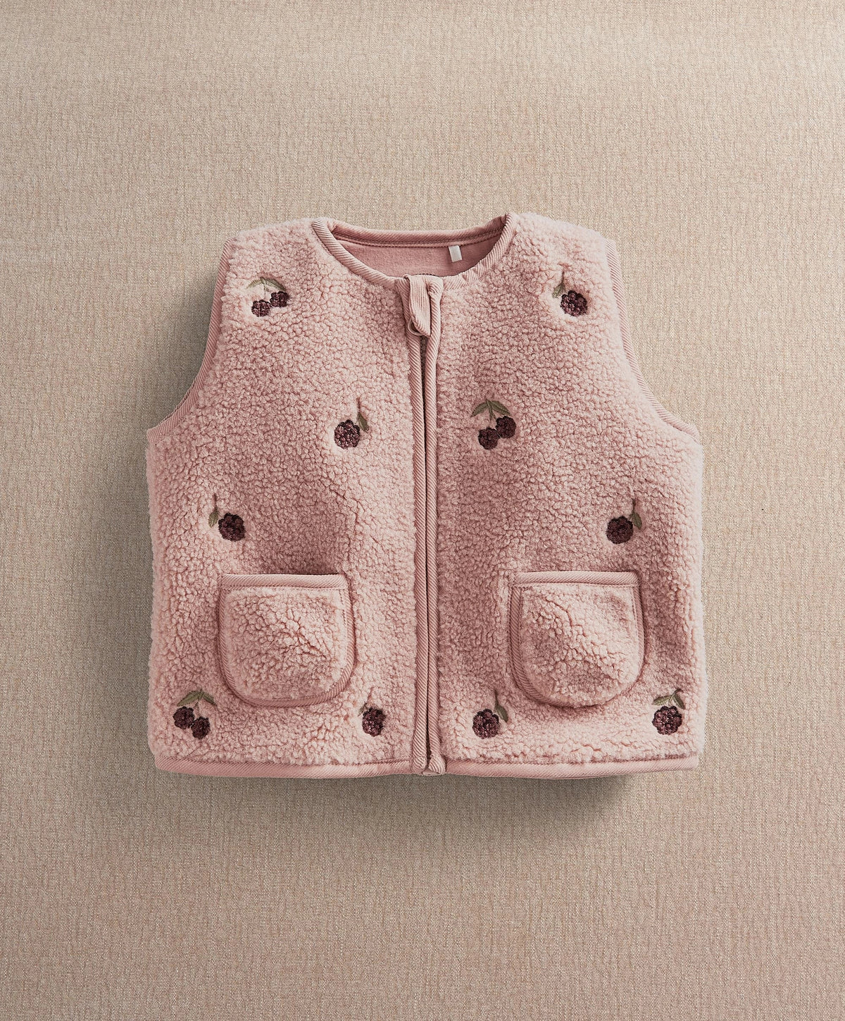 Pink fleece gilet with zipper front and two patch pockets; scattered embroidered motifs