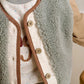 Borg gilet vest close-up: light green-gray fleece with brown edging and wood-look buttons