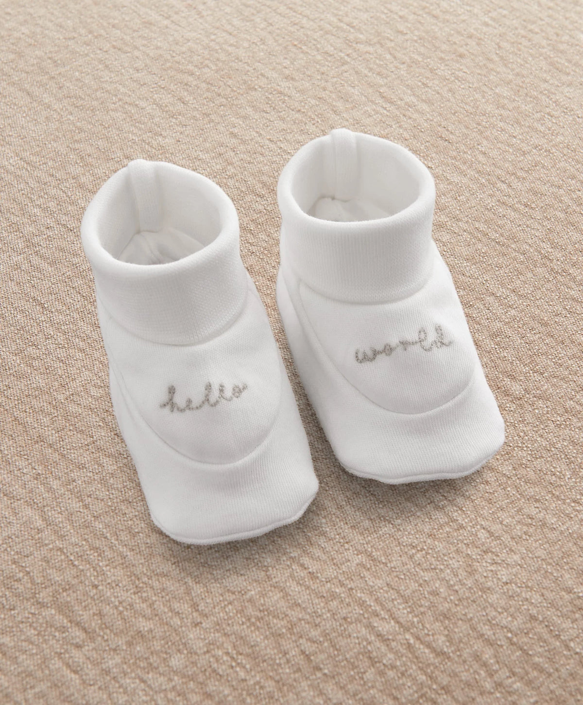 Pair of white baby booties with cursive text logo on side