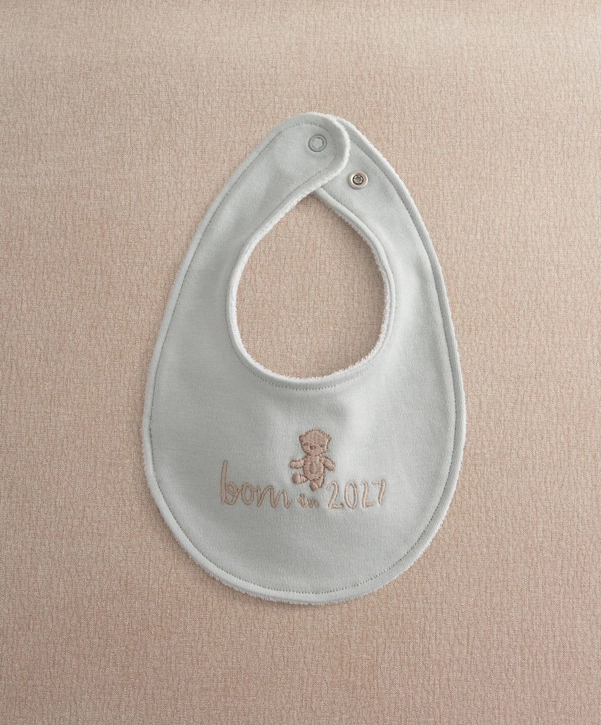 Light blue baby bib with round neck opening and embroidered teddy "Born in 2027"