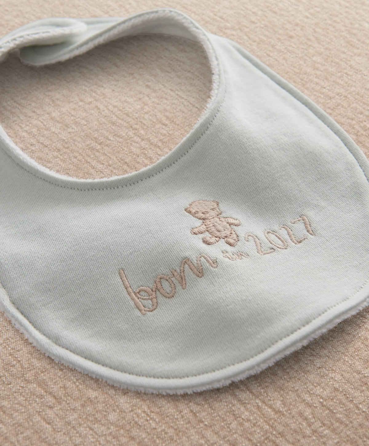 Light blue baby bib with embroidered teddy and "Born in 2027" text