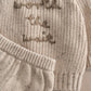 Close-up of cream knit sweater with embroidered snails and ribbed cuffs