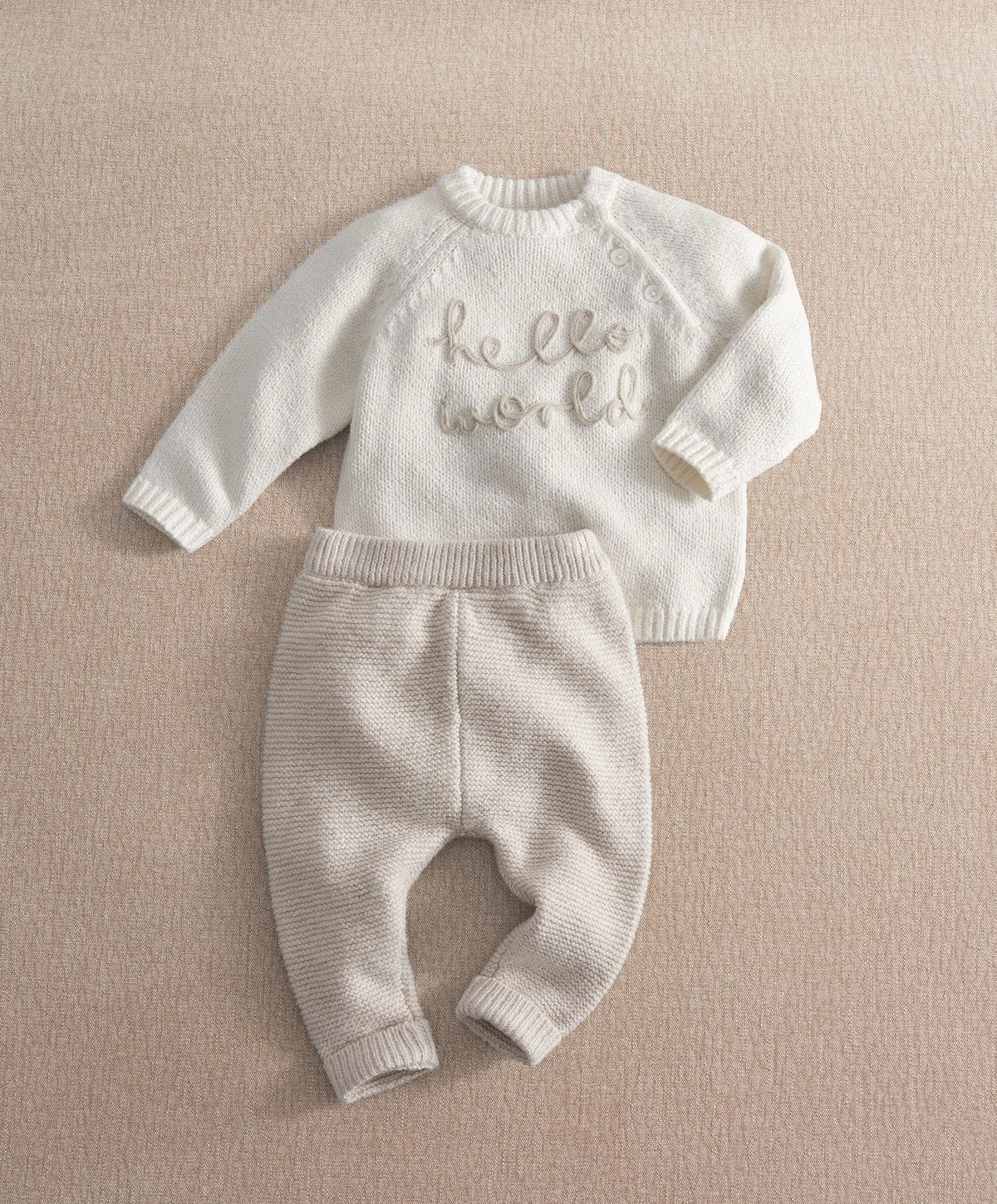 Cream knit 2-piece baby set with long-sleeve top and pants, 'hello world' embroidery, ribbed cuffs.