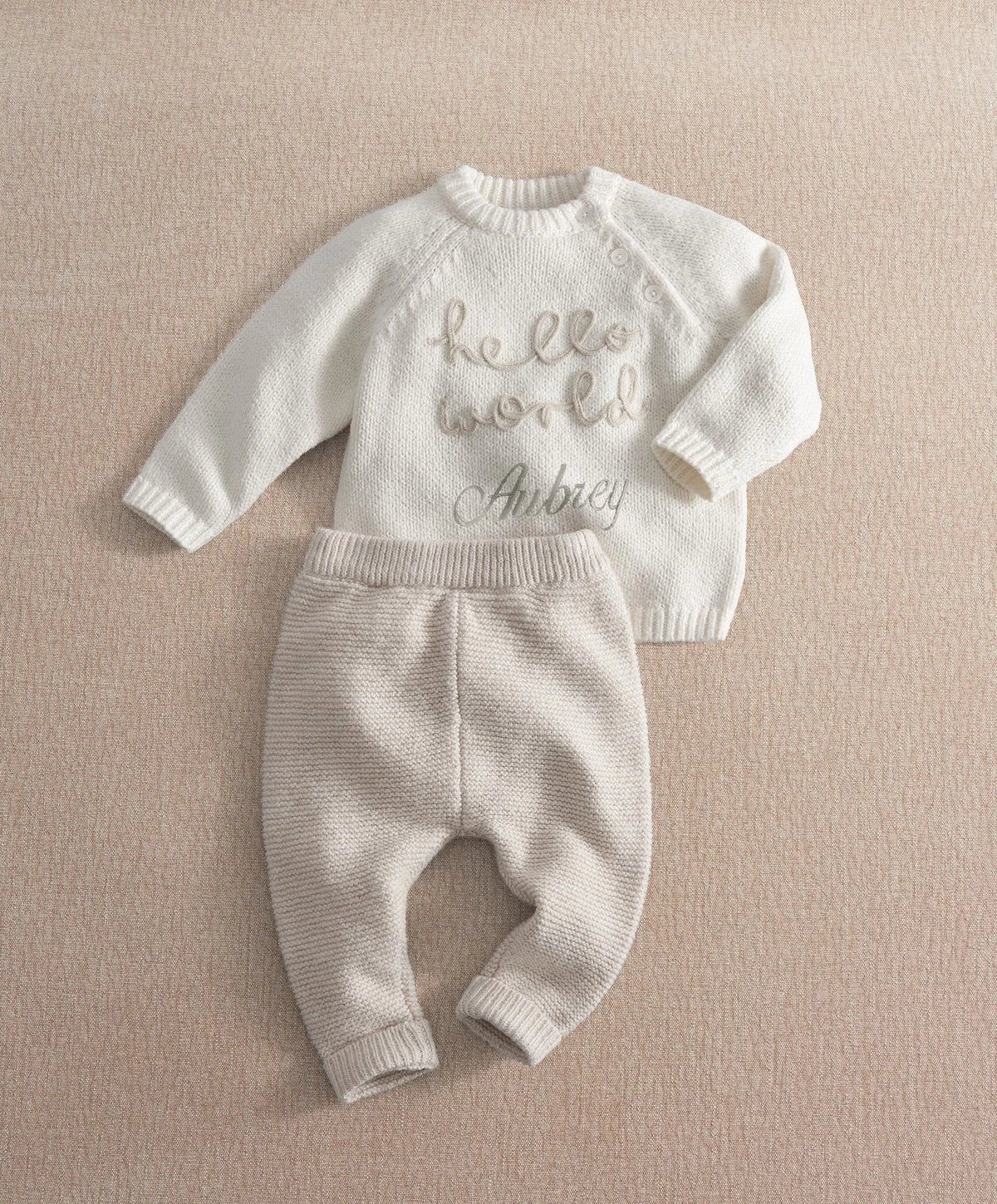 Cream knit 2-piece baby set with long-sleeve top and pants, 'hello world' and 'Aubrey' text.