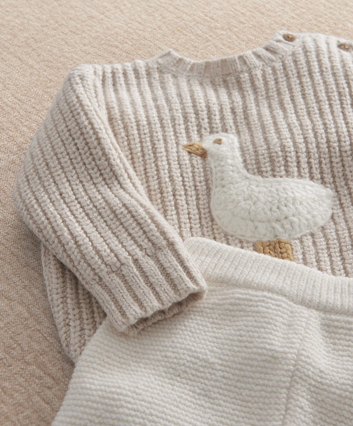Cream sweater detail with duck applique patch and ribbed knit cuffs