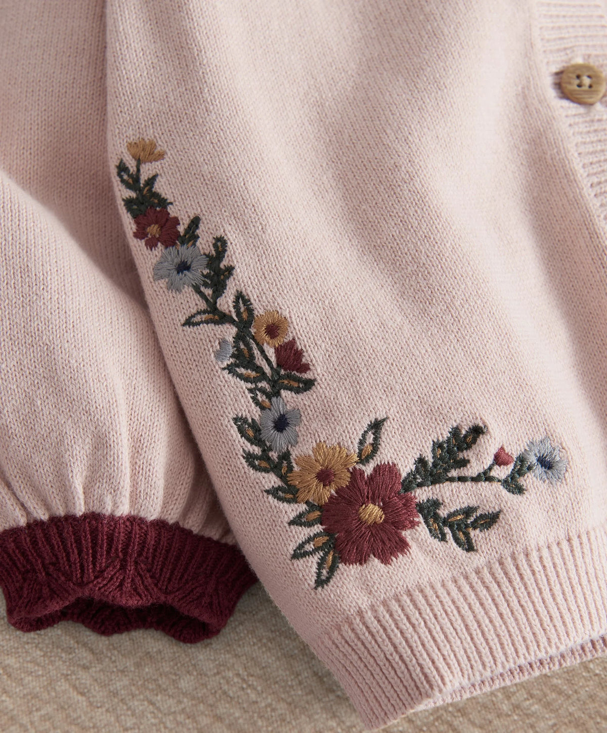 Light pink knit sleeve with floral embroidery and maroon ribbed cuff