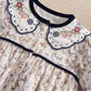 Floral romper neckline with blue scalloped trim, decorative crosses, and gathered skirt