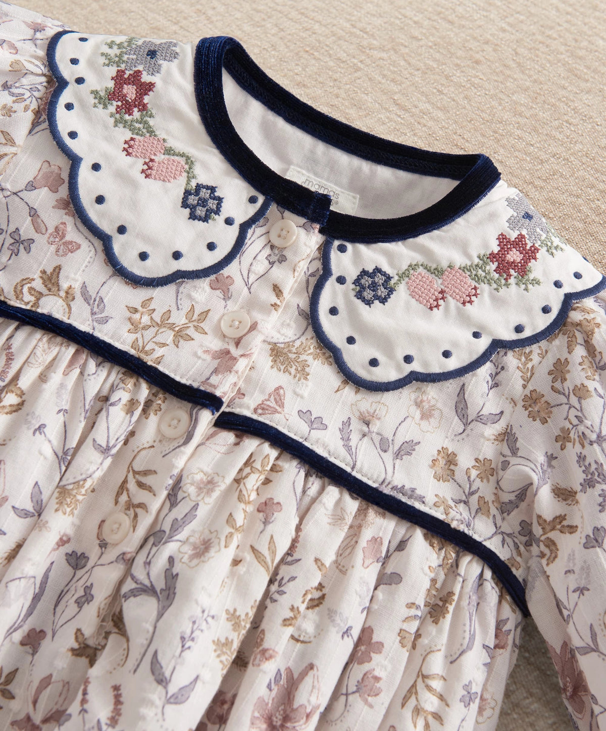 Floral romper neckline with blue scalloped trim, decorative crosses, and gathered skirt