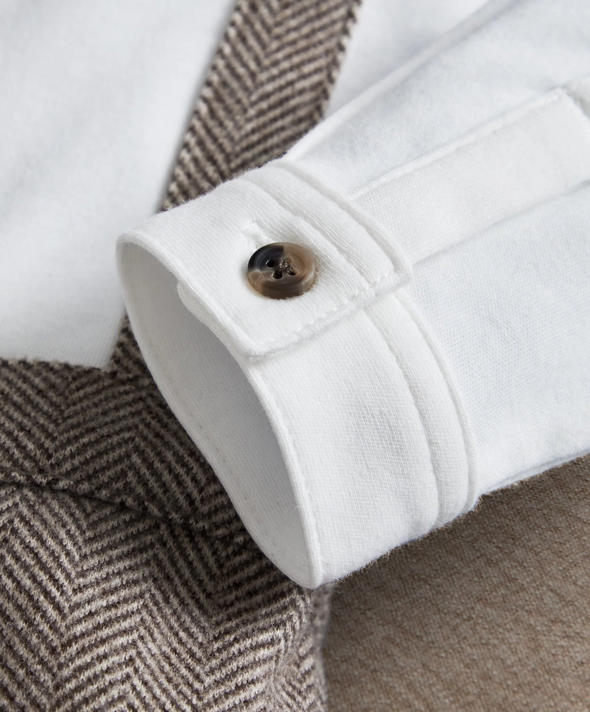 White mock-neck romper cuff with buttoned placket and dark herringbone panel