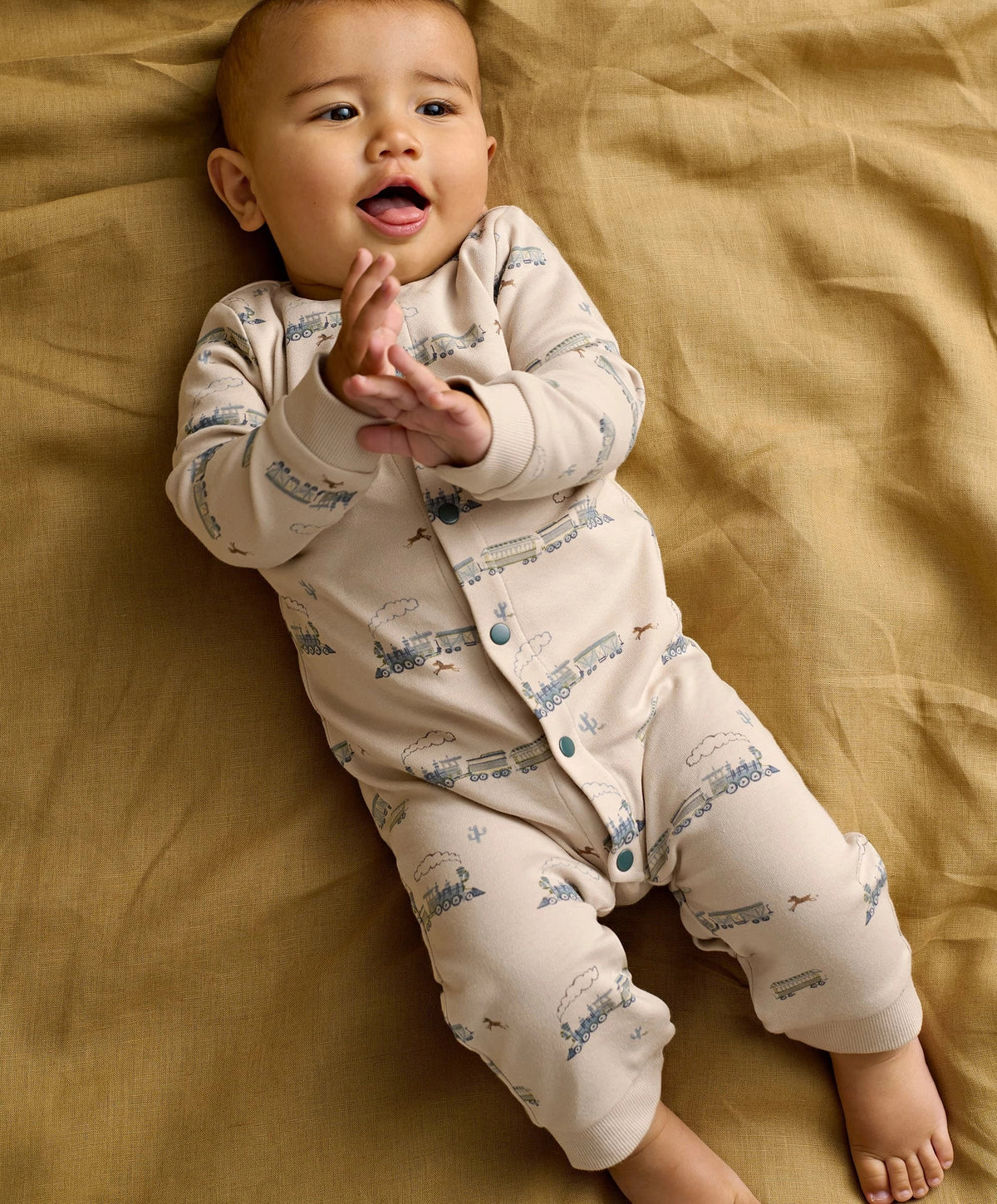 Cream long-sleeve romper with blue train pattern and turquoise snaps, baby wearing