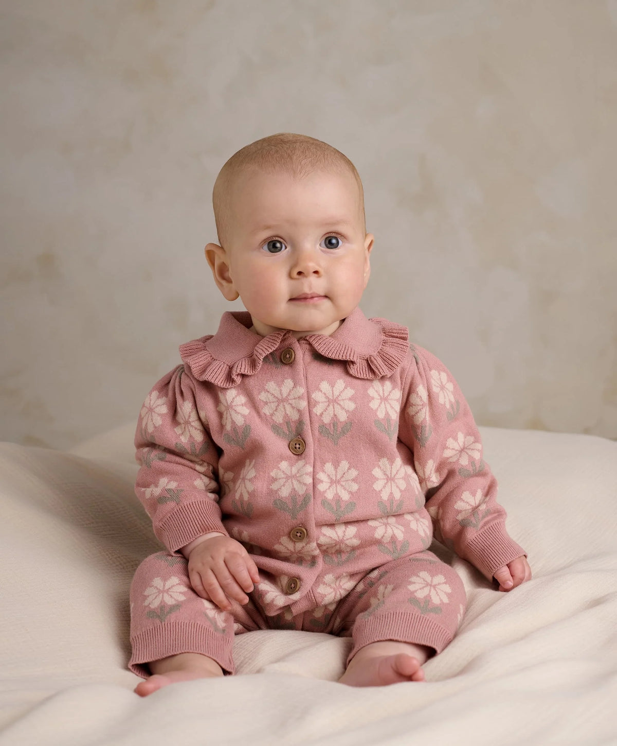 Pink floral knitted baby romper with buttoned front and ribbed collar