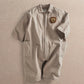 Light tan zip-front boiler suit romper with collar, bear patch, and two front pockets