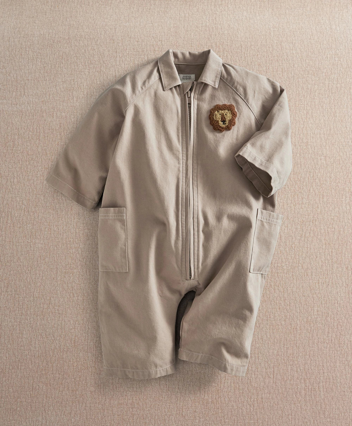 Light tan zip-front boiler suit romper with collar, bear patch, and two front pockets
