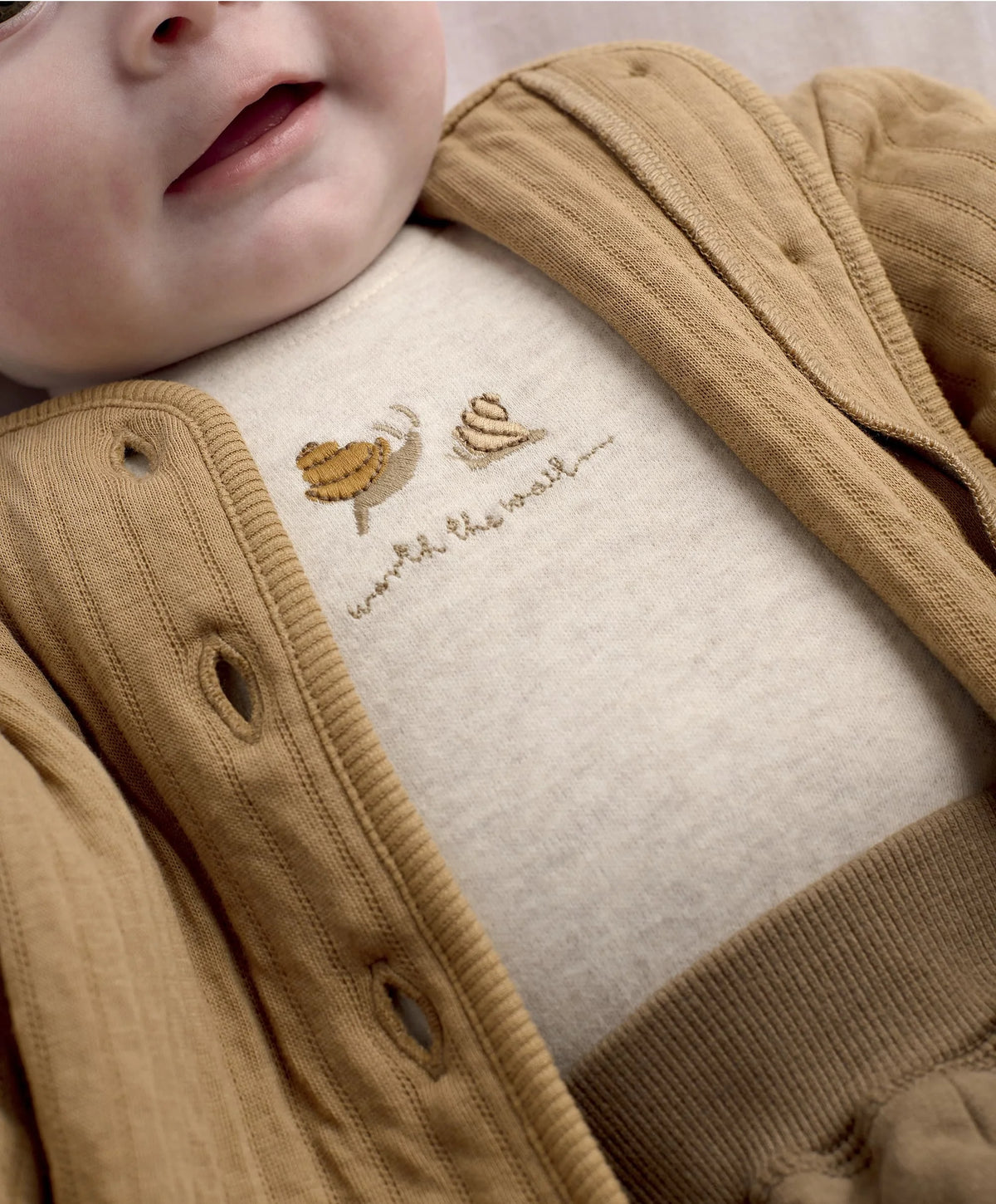 Beige embroidery on jacket, featuring snail and rainbow stitch design