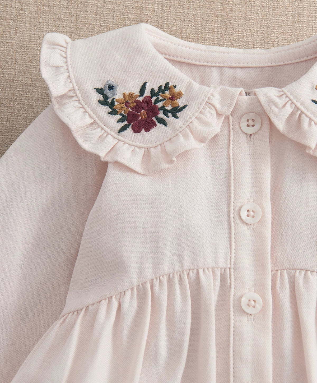 White long-sleeve top with floral yoke embroidery and button placket, ruffled neckline.