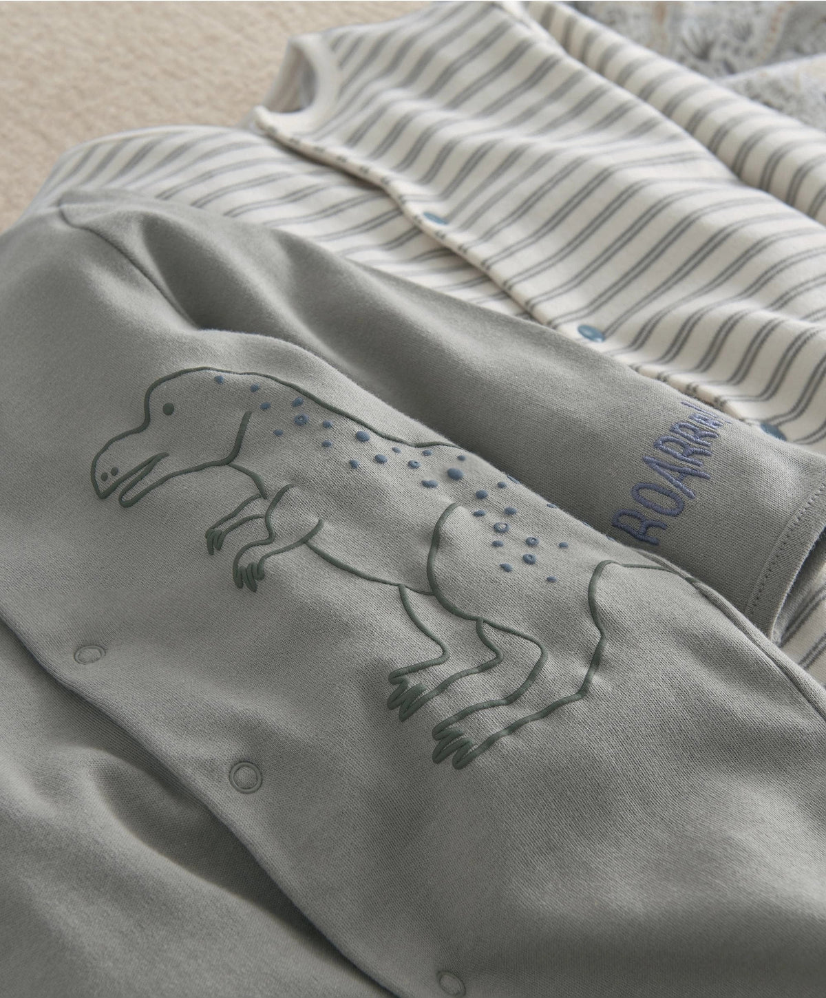 Baby sleepsuit close-up in grey with dinosaur print and ROAR text