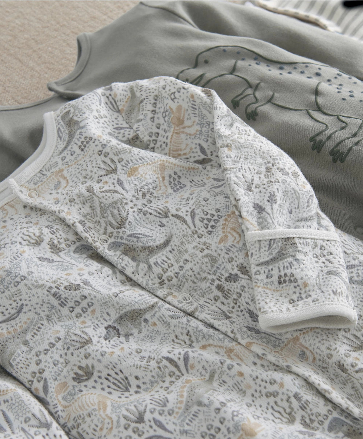 Close-up of baby sleepsuit with light dino print and ribbed cuffs