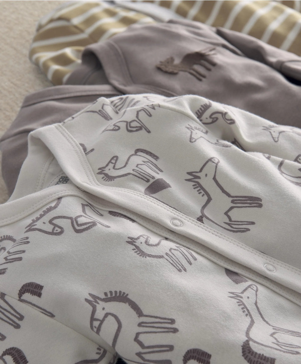White baby sleepsuit with dark horse icon print and snap button at leg opening.