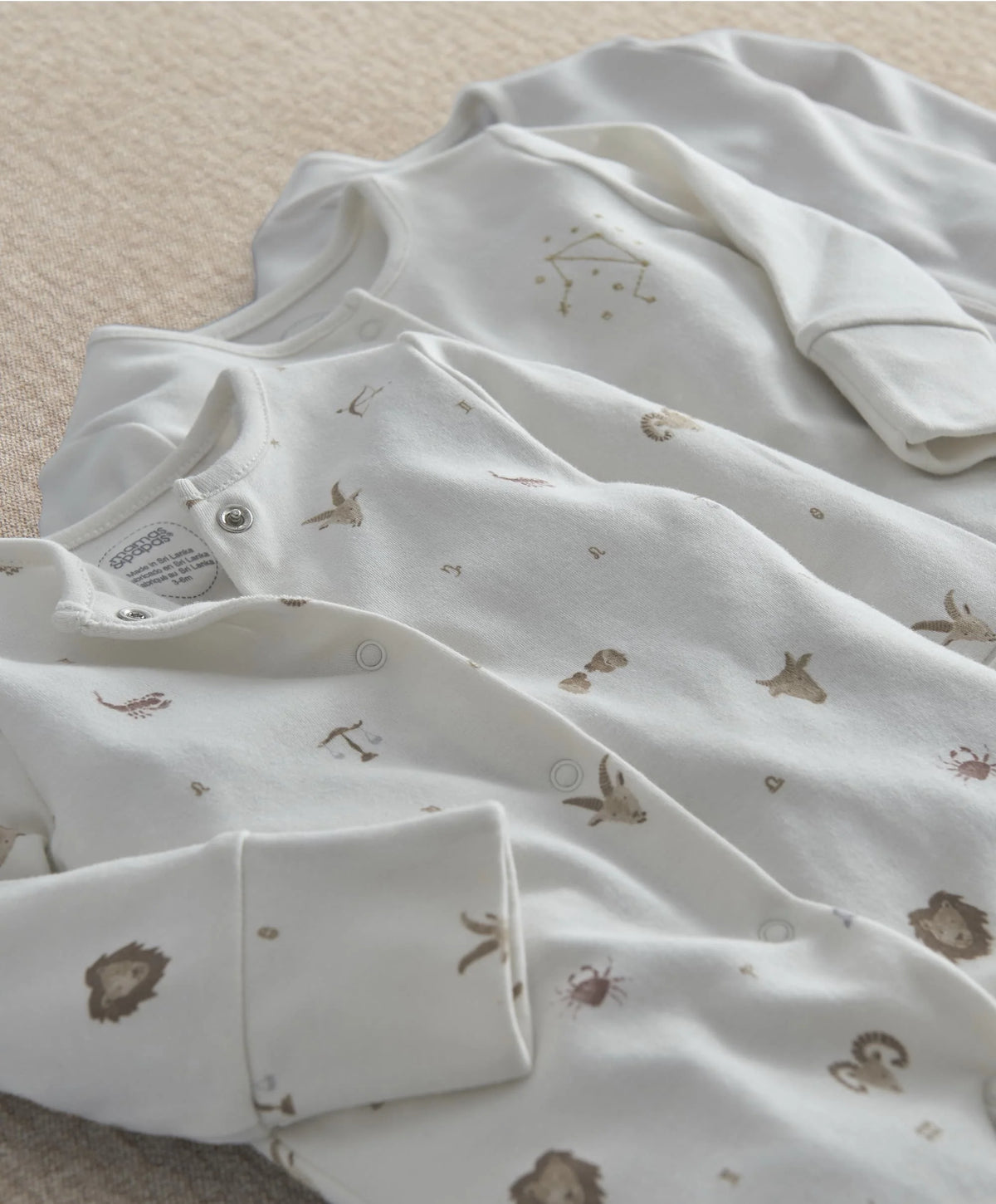 White sleepsuit with small gold symbol print and snap-button leg openings