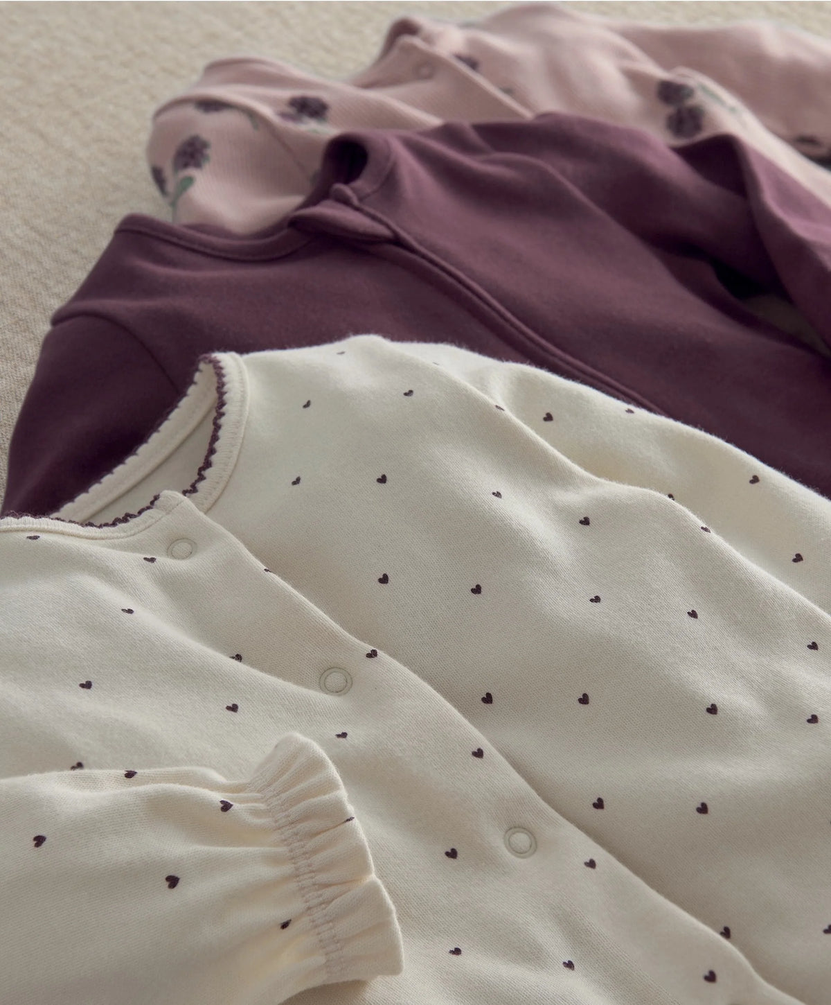 Cream baby sleepsuit with small dotted print and ruffled cuffs; plum zip