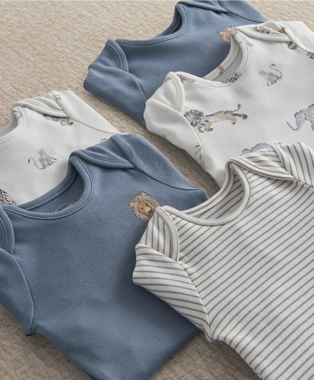Baby safari bodysuits close-up: blue solid, white animal print, and white striped bodysuits