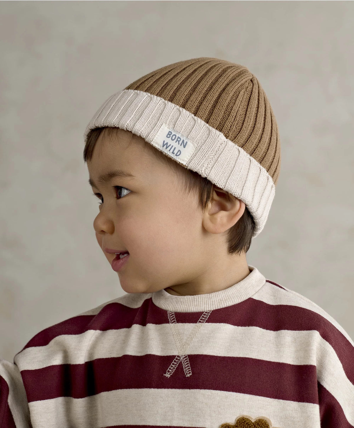 Brown knit beanie with white cuff and BORN WILD label, worn by child