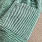Green corduroy trousers fabric close-up, vertical ribbed texture and stitched panels