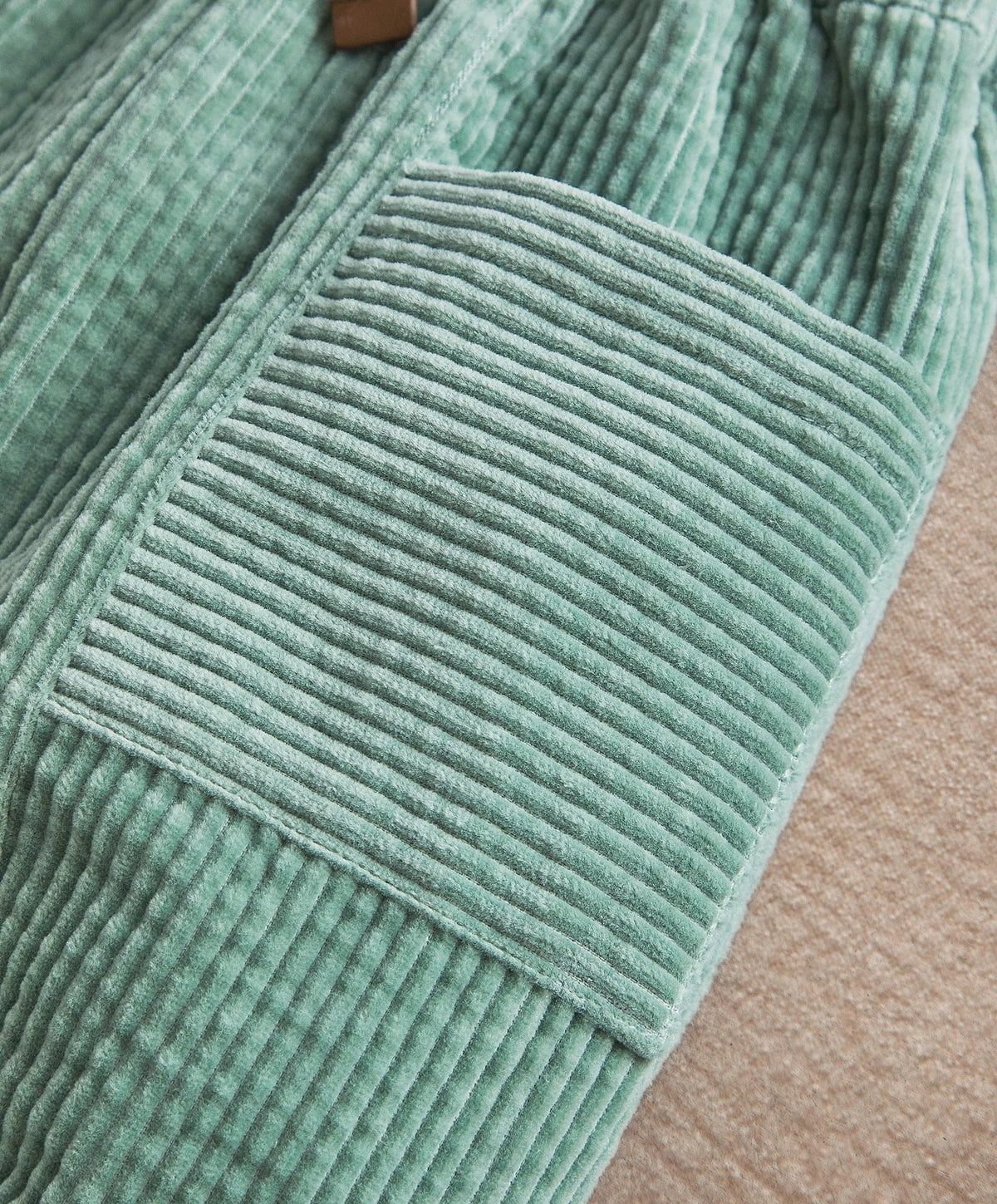 Green corduroy trousers fabric close-up, vertical ribbed texture and stitched panels
