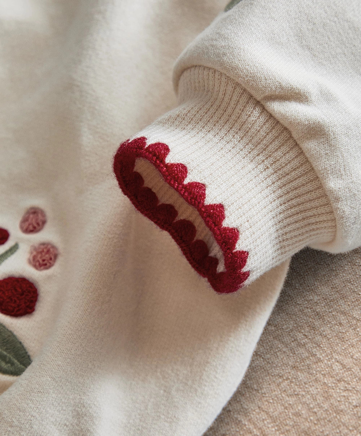 Cream sweatshirt sleeve cuff with red berry embroidery detail and ribbed knit trim