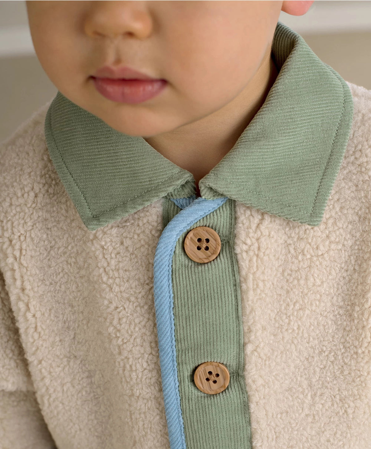 Cream borg jacket close-up with mint collar band and wooden buttons