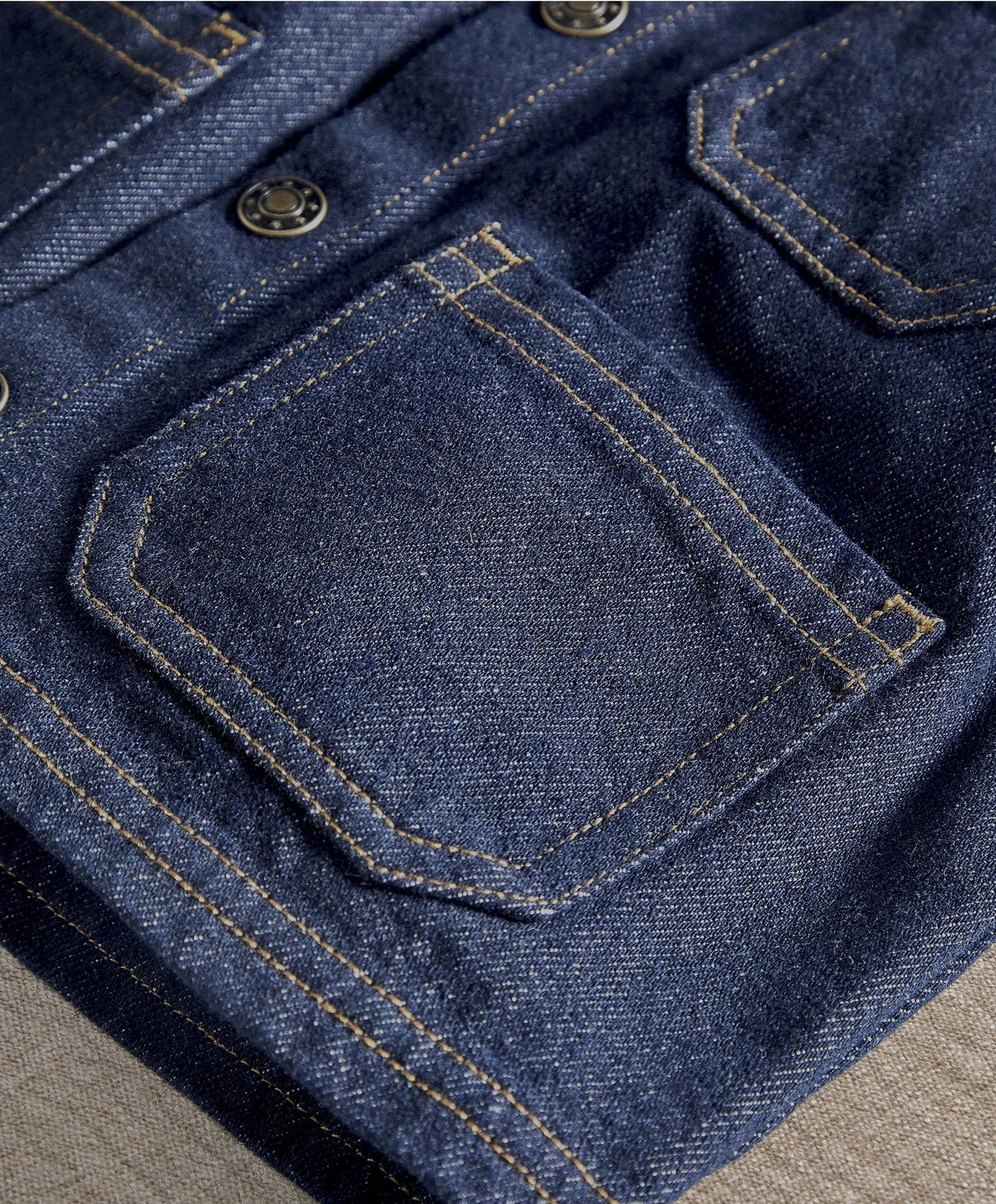 Dark blue denim jacket close-up: chest pocket with contrast topstitching and buttons