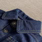 Dark blue denim jacket close-up: button placket and adjustable cuff with stitching