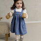Blue denim pinafore dress with chest buttons over white heart-print long-sleeve bodysuit
