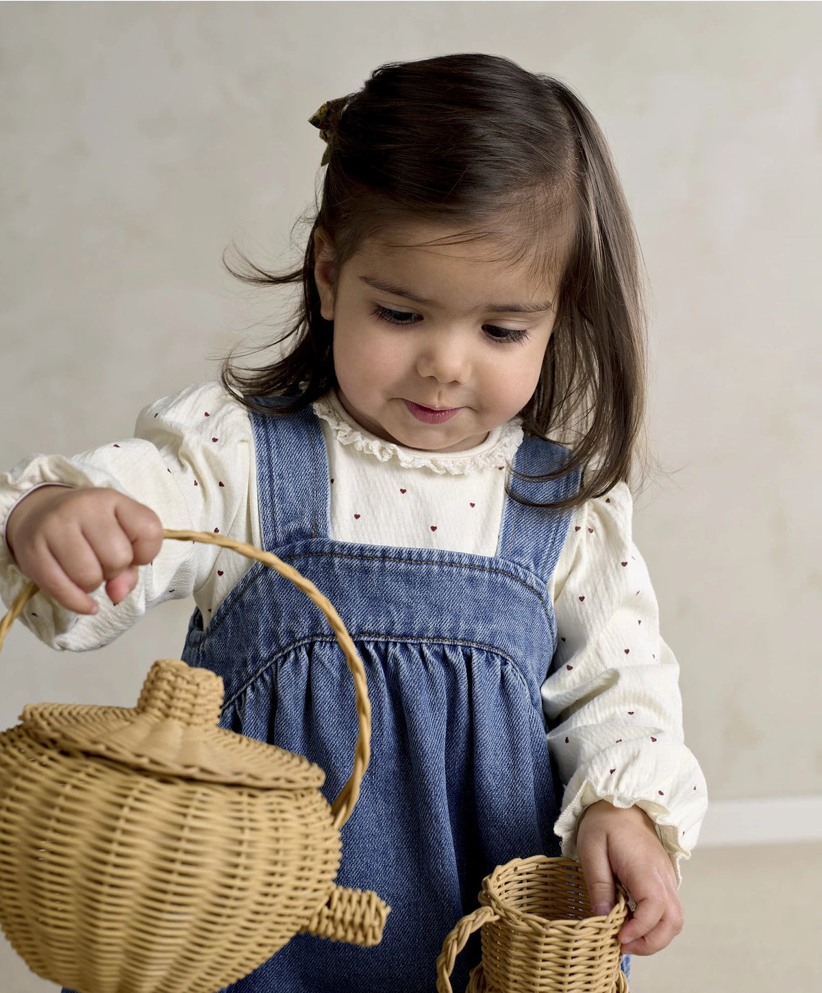Blue denim pinafore dress over white heart-print bodysuit, holding a wicker basket